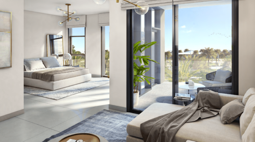 Un intérieur d'appartement moderne comprenant un salon spacieux avec un canapé beige, attenant à une chambre avec de grandes fenêtres donnant sur les collines de Dubaï, mettant en valeur une verdure extérieure luxuriante et une lumière naturelle abondante.