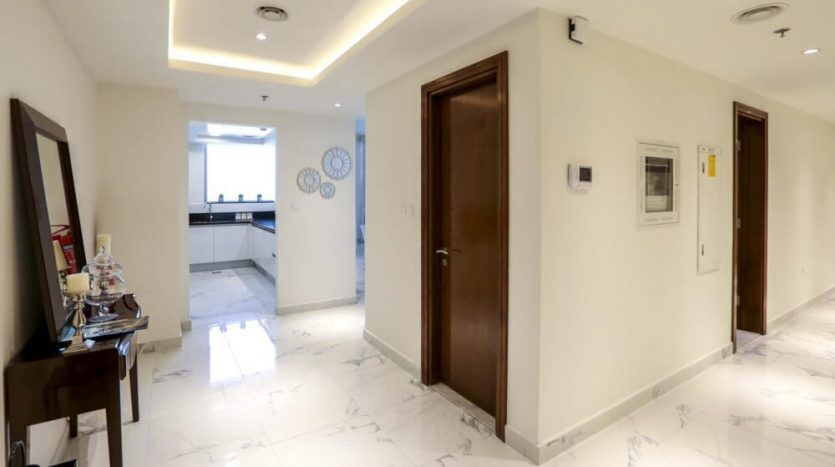 Modern hallway with marble floor, several wooden doors and elegant ceiling lighting in a Dubai villa. Decoration includes a wall clock and framed works of art.
