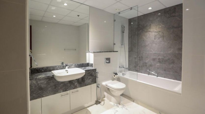 A modern bathroom in the Amna Tower in Al Habtoor City with marble finishes, including sink, basin, toilet and glass shower cubicle, all under bright lighting.