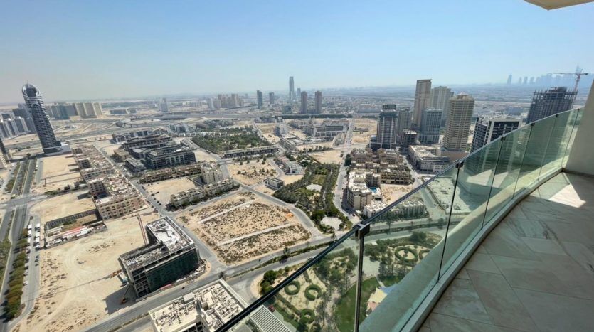 Vue aérienne depuis un balcon de grande hauteur dans Five JVC, montrant une ville tentaculaire avec des bâtiments, des rues et des terrains ouverts, sous un ciel bleu clair.