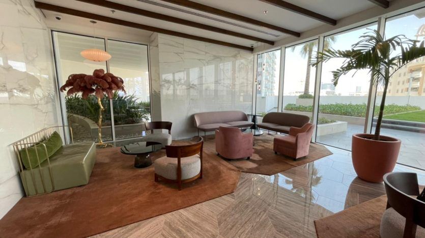 Salon moderne du Five JVC avec des murs en verre offrant une vue sur le jardin, un mélange de fauteuils verts et roses, une table basse et des intérieurs élégants avec des poutres en bois au plafond.