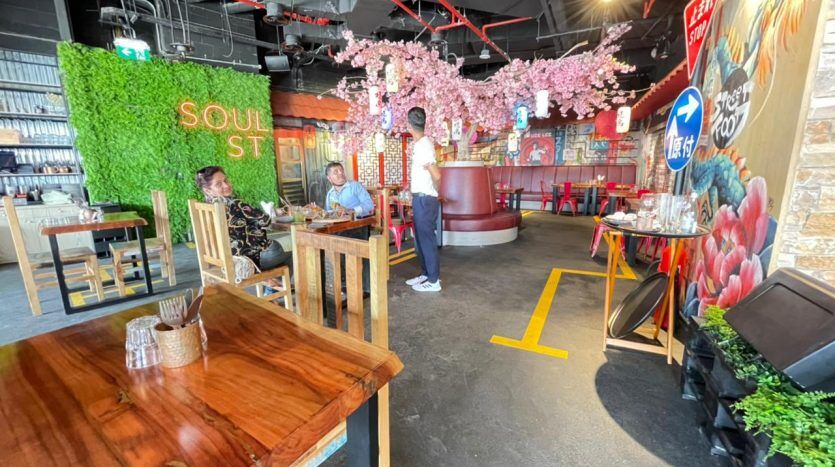 Intérieur du restaurant animé Five JVC avec une décoration éclectique, avec des fleurs de cerisier au-dessus, des peintures murales colorées et des clients assis à des tables en bois.