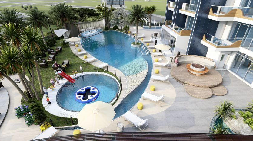 Vue aérienne d'une piscine luxueuse du complexe Samana Waves Dubaï, entourée de palmiers, de chaises longues et d'une architecture moderne, avec des gens profitant de la journée ensoleillée.