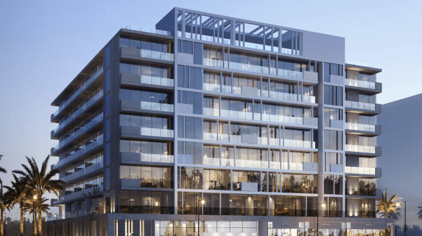 Bâtiment moderne de plusieurs étages à Dubaï au crépuscule, doté de fenêtres et de balcons éclairés, avec des piétons visibles au niveau de la rue et des palmiers flanquant la structure.