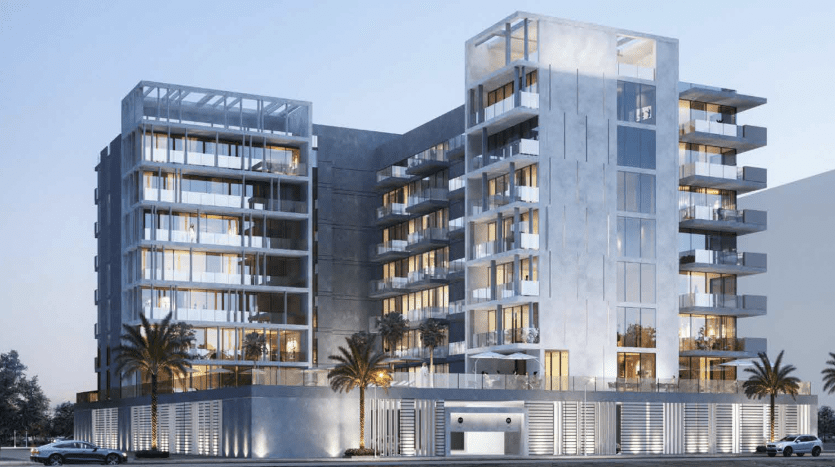 Immeuble résidentiel moderne de plusieurs étages éclairé le soir avec des balcons, de grandes fenêtres et des voitures garées à l'extérieur, parfait pour les opportunités d'investissement à Dubaï.