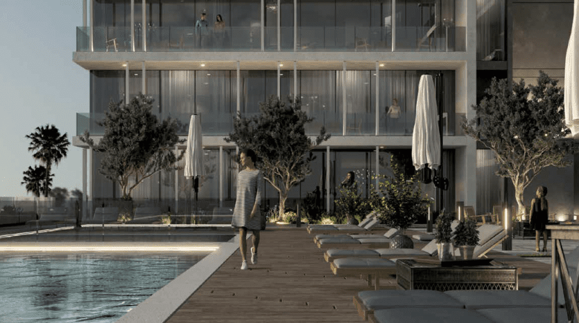 Une scène moderne au bord d'une piscine au crépuscule à Dubaï, mettant en vedette une personne marchant le long d'une terrasse en bois, entourée de chaises longues et d'arbres, avec un élégant bâtiment à plusieurs étages en arrière-plan.