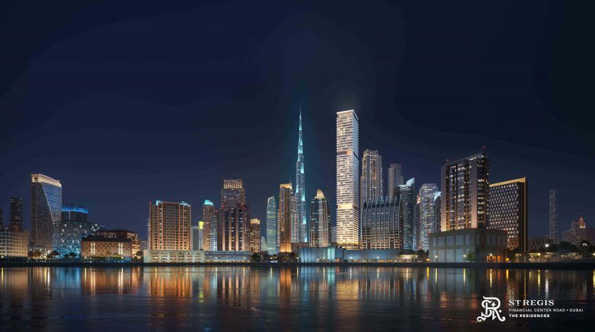 Night view of modern Dubai reflected in calm waters, with illuminated skyscrapers and residential buildings under a clear sky.