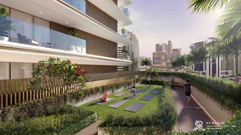A serene outdoor yoga session in a lush garden, with four people practicing on mats. The landscape includes flowering plants and modern high-rise buildings in Dubai in the background, under a clear sky.
