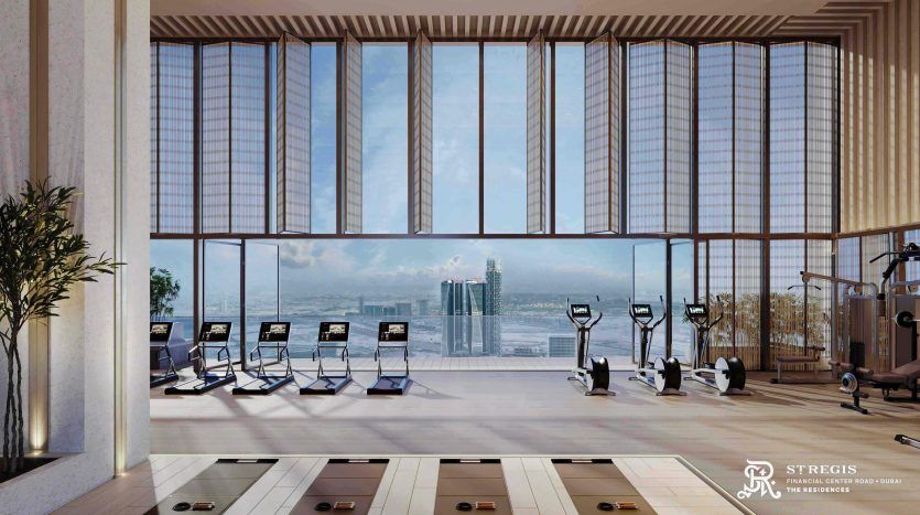 Luxurious indoor gym with large picture windows offering panoramic views of Dubai's city skyline. Includes treadmills, bikes and weights, with natural light accentuating the modern decor.