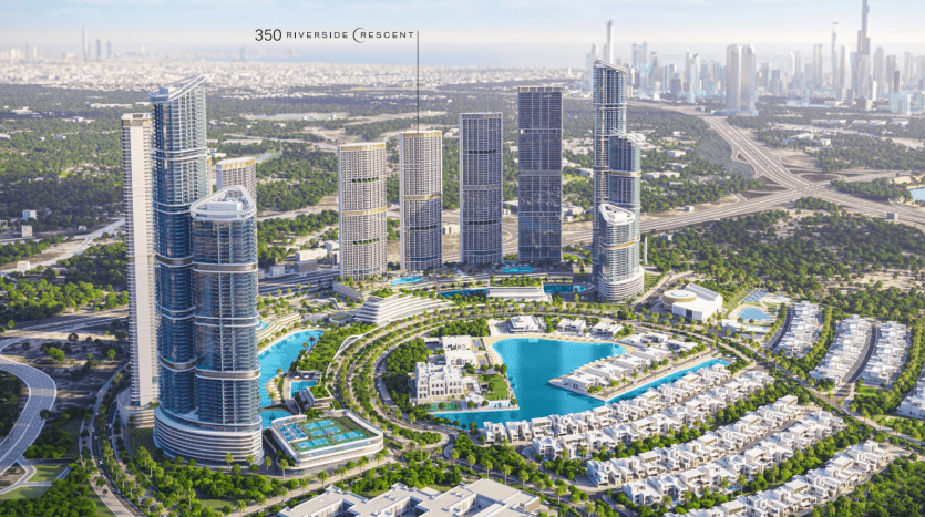 Aerial view of a modern urban development featuring high-rise buildings, a large artificial lake, lush green spaces and residential villa areas in Dubai, with a city skyline in the background.