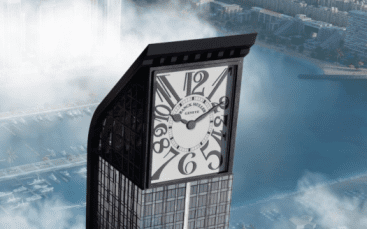 A high-rise building with a large clock face integrated into its top, overlooking a coastal city of Dubai partially obscured by morning fog.