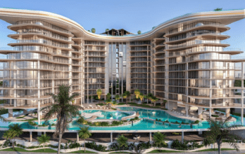 Modern, curvilinear multi-storey residential buildings flanking a central tower, with lush landscaping and a luxurious swimming pool, all set against a clear, sunny Dubai sky.