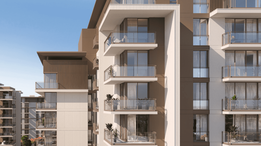 Exterior view of a modern apartment building in Dubai featuring several balconies with glass balustrades, plants and outdoor furniture under a clear blue sky.