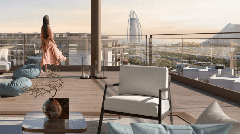 A woman in a flowing dress stands on the spacious balcony of a luxury apartment in Dubai, overlooking a cityscape with iconic skyscrapers, next to elegant patio furniture and decorative elements.