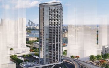 A sleek, modern skyscraper stands amidst a cityscape of high-rise buildings and green spaces. The building is named the Franck Muller Vanguard London Gate and is surrounded by a mix of commercial and residential areas near a body of water.