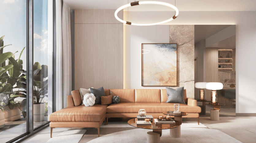 A modern living room with a beige leather sectional sofa and abstract artworks on the wall is illuminated by a round ceiling light. The Legado Prescott glass coffee table displays decorative objects, while large windows highlight the green plants outside, bathing the space in natural light.