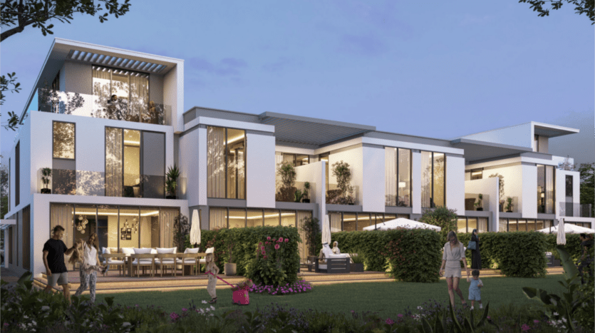 Una moderna villa blanca de varias plantas en las islas Damac tiene grandes ventanales y terrazas, rodeada de exuberante vegetación. La gente disfruta del jardín, con los adultos cerca de un comedor al aire libre y los niños jugando en la hierba. El cielo es de un azul suave al atardecer.