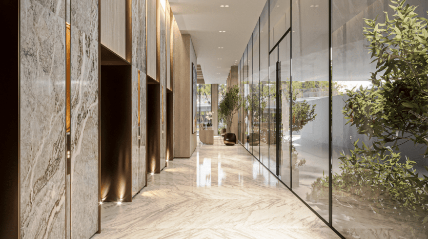 Luxurious, modern hallway with marble floors and walls, glass partitions and lush greenery. Subdued ceiling lighting creates a warm ambience. The space features sleek design elements and indoor plants.