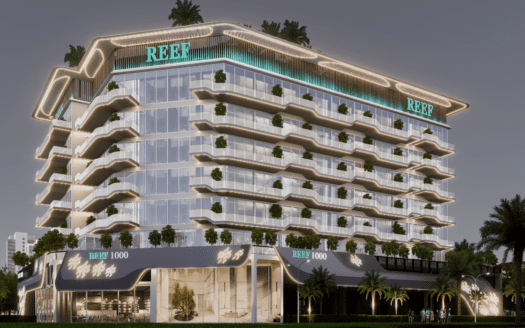 Futuristisches Gebäude bei Nacht namens REEF mit einer Leuchtreklame. Es besteht aus mehreren Stockwerken mit Glasfenstern und Balkonen, die mit kleinen Bäumen geschmückt sind. Im Hintergrund sind Palmen und Gebäude der Stadt unter einem dunklen Himmel zu sehen.