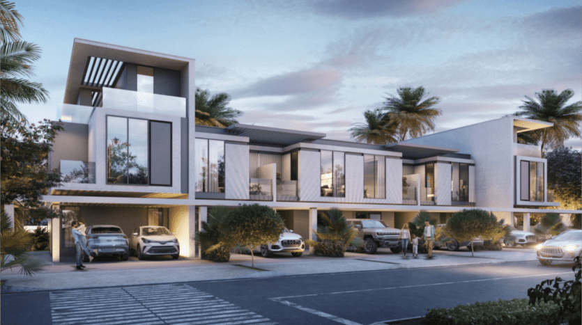 Al atardecer, el complejo de modernas casas adosadas de las islas Damac presenta grandes ventanales y balcones enmarcados por palmeras. Varios coches aparcados bordean la calle mientras la gente pasea entre la exuberante vegetación, creando un ambiente sereno pero vibrante.