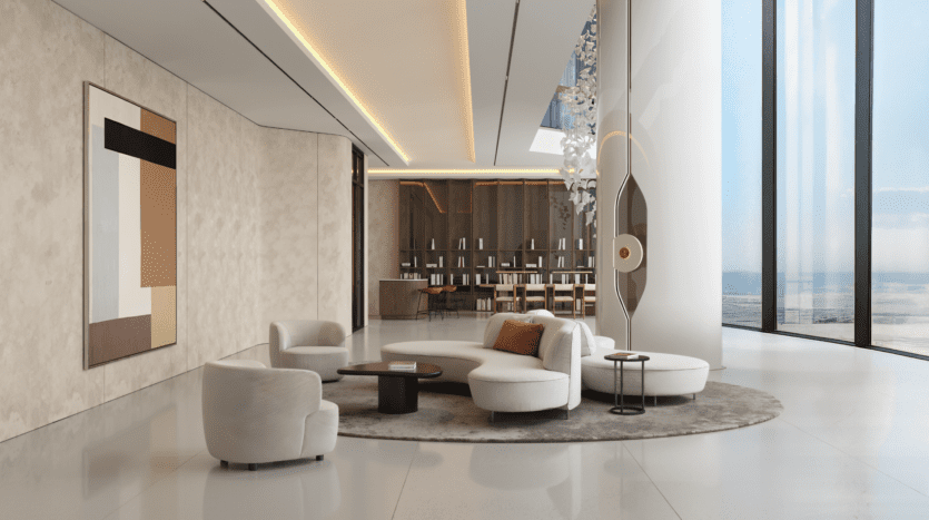 A modern, elegant living room with cream-colored curved sofas, a round carpet, abstract wall art, bay windows offering ocean views and a large sculpture near an elegant bar in the background.