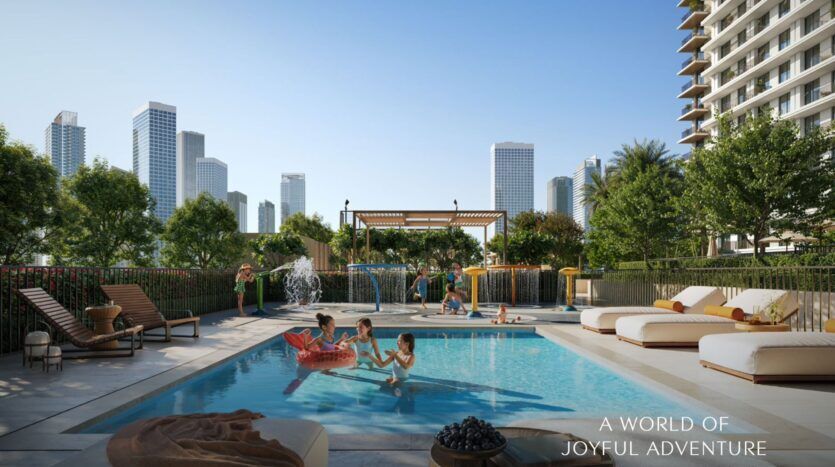Des enfants jouent dans une petite piscine extérieure avec des structures gonflables à Creek Bay, entourés de chaises longues, d'arbres et de verdure. De grands immeubles urbains s'élèvent à l'arrière-plan sous un ciel bleu clair. Le texte se lit comme suit : "A WORLD OF JOYFUL ADVENTURE.