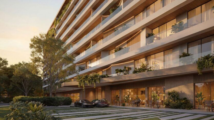 Lunaya Terraces est un immeuble d'appartements moderne de plusieurs étages, doté de grands balcons, d'espaces verts abondants et de baies vitrées. Deux voitures de luxe sont garées devant, tandis que des coins salon en plein air et un aménagement paysager luxuriant entourent le site.
