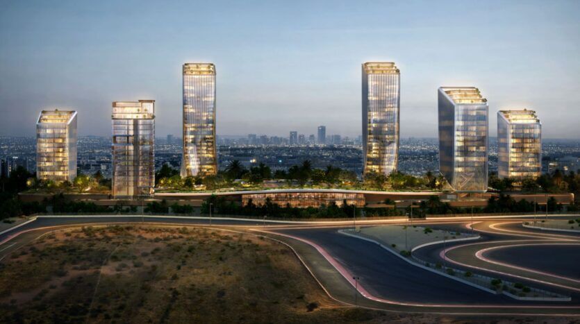 Six gratte-ciel modernes en verre du quartier O1NE, illuminés à la tombée de la nuit, se dressent au milieu de la verdure, avec la silhouette de la ville en arrière-plan et des routes sinueuses au premier plan.