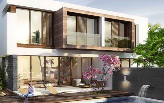 Une maison moderne de deux étages à Damac Hills avec de grandes fenêtres et des touches de bois, entourée d'une verdure luxuriante. Un arbre à fleurs roses fleurit au bord d’une piscine avec une personne se relaxant sur une chaise longue.