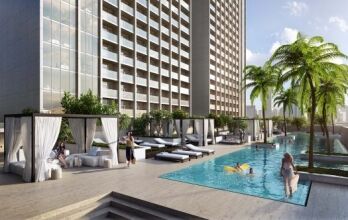 Sterling Dubai luxury hotel pool area with sun loungers and cabanas, surrounded by tall buildings under a clear sky. People relax and swim in a sunny, tranquil setting.