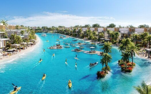 Le grand lagon bleu clair de Damac Islands 2 est entouré de villas modernes, de palmiers et de plages de sable, où les gens font du kayak, du paddleboard et se détendent sur des plates-formes flottantes sous un ciel d'un bleu éclatant.