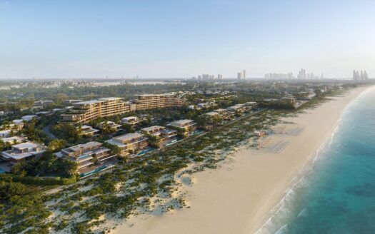 Vue aérienne de la station balnéaire Four Seasons Private Residences, dont les bâtiments modernes sont entourés de verdure, d'une plage de sable et d'un océan bleu. Des chaises longues et des parasols bordent le rivage ; la silhouette d'une ville est visible à l'arrière-plan.