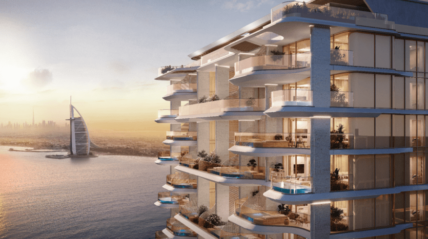 Un condominium balnéaire moderne de plusieurs étages, doté de balcons spacieux et de petites piscines. Alors que le soleil se couche sur l'océan, le Vitalia Palm Jumeirah se dresse au loin, son architecture distinctive en forme de voile créant une silhouette à couper le souffle.