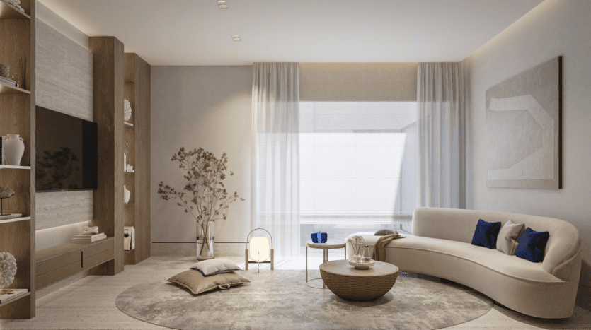 Un salon moderne à Vitalia Palm Jumeirah comprend un canapé beige incurvé, une table basse ronde et un tapis rond. Des étagères allant du sol au plafond abritent une télévision et des objets de décoration. Une grande fenêtre avec des rideaux transparents laisse entrer la lumière naturelle, tandis que des œuvres d'art minimalistes et une petite plante complètent le look.