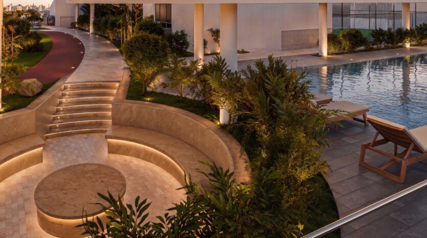 Espace extérieur moderne au crépuscule au Beverly Crown by HMB, comprenant un coin salon circulaire en contrebas, des marches éclairées, une végétation luxuriante, une piscine, des chaises longues et une piste de course jouxtant un bâtiment contemporain.
