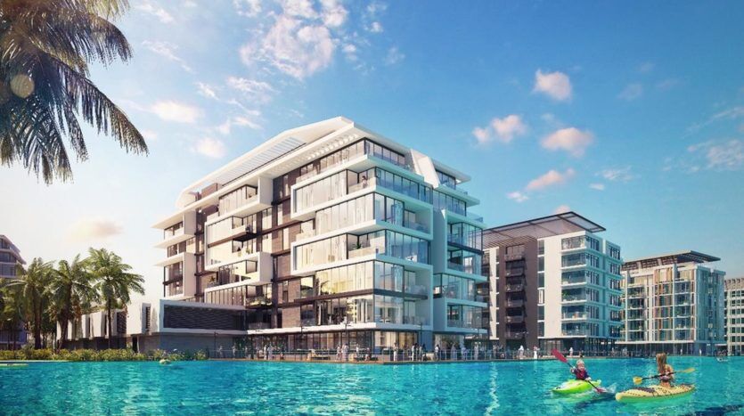 Une copropriété moderne au bord de l'eau avec balcons, entourée d'autres bâtiments, de palmiers et d'une piscine bleu clair avec des kayakistes.