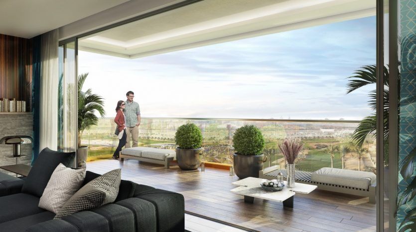 Un couple marchant sur un balcon spacieux dans un luxueux appartement de Dubaï, surplombant un vaste paysage verdoyant, visible à travers de grandes fenêtres en verre.