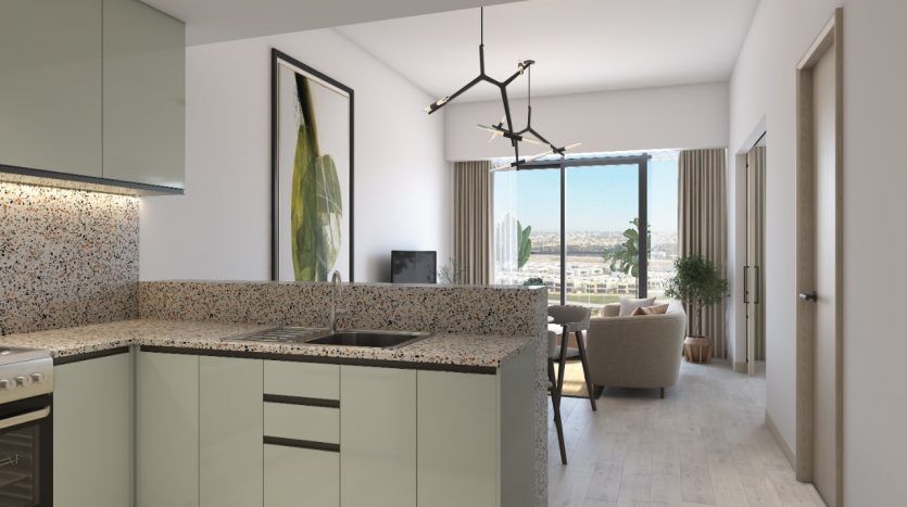 Cuisine moderne avec armoires vert menthe et comptoirs mouchetés, offrant une vue sur un salon lumineux et le paysage urbain de Dubaï à travers une grande fenêtre.