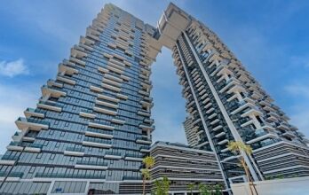 Bâtiments architecturaux modernes avec un pont aérien unique reliant deux tours de grande hauteur à Dubaï, sur un ciel bleu clair. La conception comprend plusieurs balcons et une structure en couches.