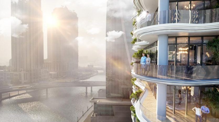 Une terrasse extérieure sereine et ensoleillée d'un appartement de grande hauteur à Dubaï surplombant la rivière d'une ville et d'autres gratte-ciel, avec des personnes profitant de la vue.