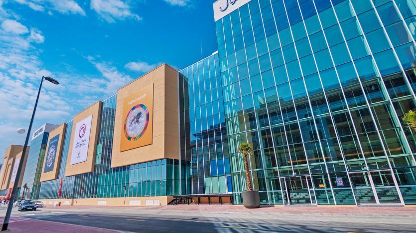 Dubai's modern urban street featuring a lively, contemporary building with large glass windows, colorful wall panels and commercial logos under a clear blue sky.