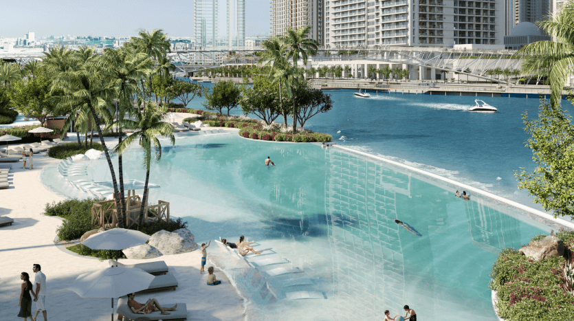 Un complexe urbain luxueux avec une grande piscine bleu clair, des zones sablonneuses avec des chaises longues et d'imposants gratte-ciel en arrière-plan au bord d'une rivière à Dubaï.