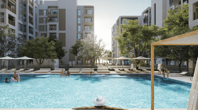 Une scène animée de piscine extérieure dans un complexe résidentiel de Dubaï, avec des gens nageant et se prélassant sous des parasols, entourés de bâtiments modernes et de verdure.
