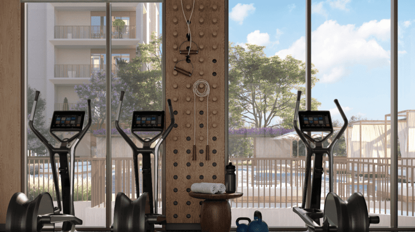 Un intérieur de salle de sport moderne dans un appartement à Dubaï, avec lumière naturelle présentant deux tapis roulants, un banc d'haltérophilie, des haltères et un mur d'escalade, donnant sur un