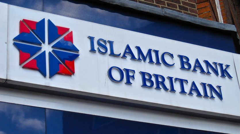 Une pancarte comportant le logo et le nom « Banque islamique de Grande-Bretagne » monté sur un mur de briques. Le logo est un dessin en étoile bleue et rouge, symbolisant leur investissement à Dubaï.