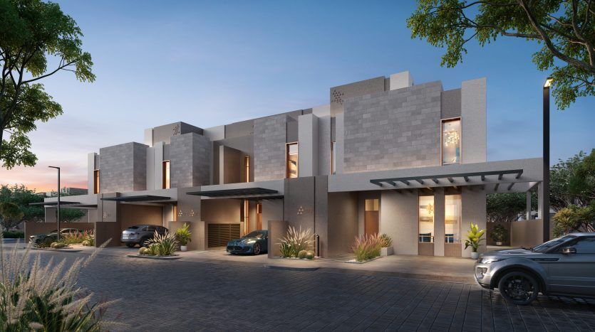 Villas résidentielles modernes à Dubaï avec des intérieurs éclairés et un éclairage extérieur au crépuscule, avec des voitures garées, des jardins bien entretenus et un ciel dégagé.
