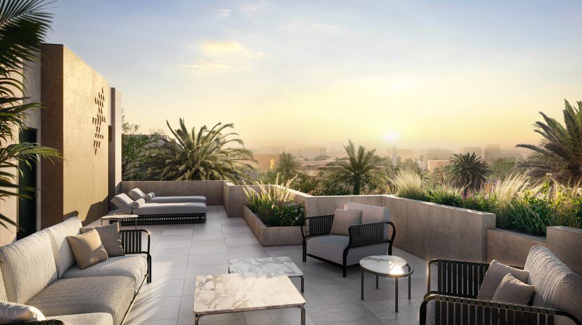 Luxueux toit-terrasse au coucher du soleil avec mobilier d'extérieur moderne, plantes en pot luxuriantes et vue panoramique sur les toits de Dubaï partiellement obscurcis par la verdure.