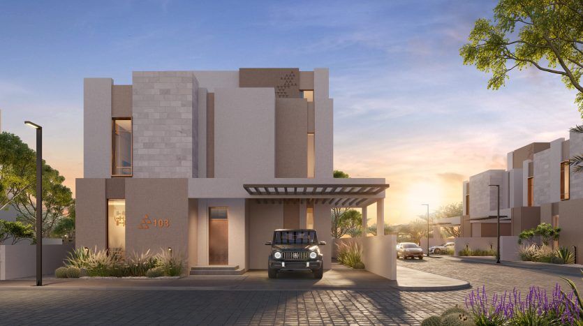 Une maison moderne avec un toit plat et une façade beige au coucher du soleil, située dans le quartier immobilier privilégié de Dubaï. Une voiture est garée sous l'allée couverte. Un aménagement paysager bien entretenu met en valeur