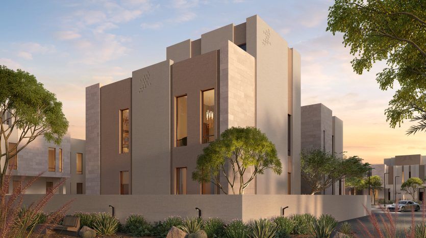 Bâtiment résidentiel moderne au design minimaliste avec des tons neutres, de grandes fenêtres et entouré d'un aménagement paysager désertique avec de petits arbres et arbustes sous un ciel coucher de soleil. Idéal comme opportunité d’investissement à Dubaï.