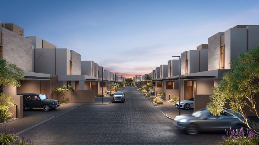 Rue résidentielle moderne au crépuscule avec des maisons symétriques, des voitures dans les allées et un ciel rose et bleu vif. Les arbres décoratifs et l'aménagement paysager rehaussent l'atmosphère tranquille de la banlieue, qui rappelle un quartier chic de Dubaï.